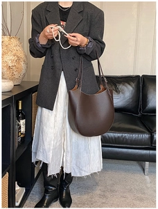 Foto lifestyle di borsa hobo in pelle marrone scuro indossata con blazer grigio e gonna