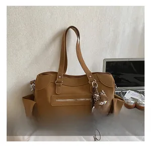 Detail view of brown tote bag with decorative zippers and plush animal charm