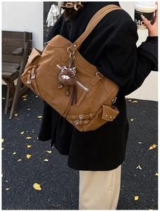 Detail of large brown vintage tote bag with metal zippers and plush charm on black coat