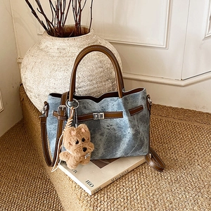 Detail of vintage denim tote bag with brown leather handles and plush puppy charm