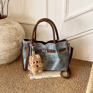 Detail of blue denim tote bag featuring brown leather trim and cute plush puppy charm