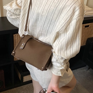 Close-up of brown leather crossbody bag featuring silver studs and metal lock detail