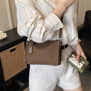 Close-up of brown textured leather Boston bag with silver metal lock and adjustable strap