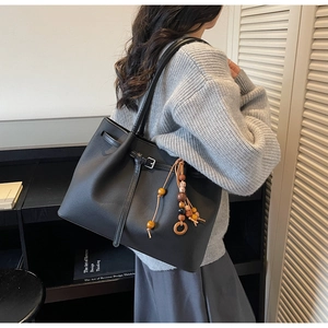 Detail of black leather tote bag featuring ethnic wooden bead charm and strap buckle