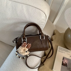 Detail of dark brown mini Boston bag with plush dog charm on beige sofa