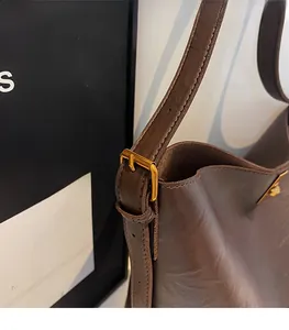 Detail of adjustable strap with matte gold buckle on brown leather bucket bag