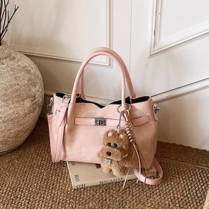 Detail of light pink tote bag featuring a silver twist lock and a brown teddy bear charm