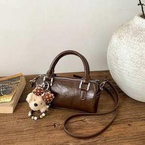 Detail of dark brown cylinder bag with plush puppy charm on a rustic wooden table