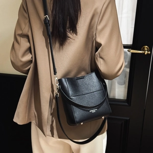 Detail der schwarzen Eimer-Tasche mit Lychee-Narbung, silbernen Füßen und Logo am Model