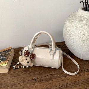 Top view of beige leather cylinder bag with bear charm on dark wood surface