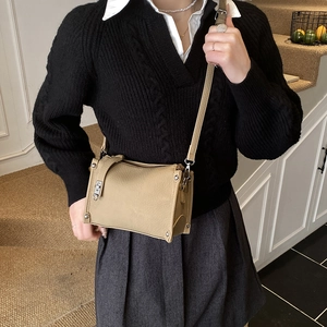 Detailed view of a khaki Boston bag with silver buckle worn over a black knit sweater