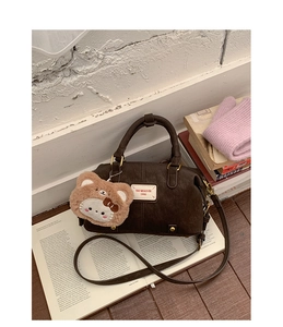 Detail of dark brown leather baguette bag with textured finish and cute plush bear charm