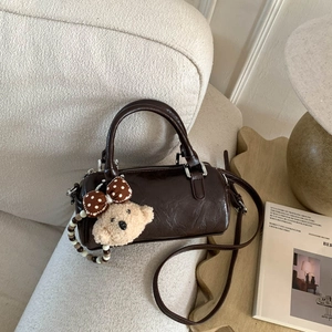 Macro detail of deep brown Boston barrel bag with glossy texture and teddy bear charm