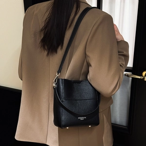 Details der Eimer-Handtasche aus Litschi-Leder mit Metallfüßen und Markenschrift