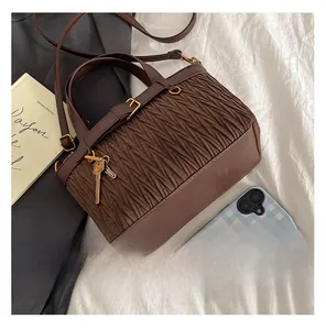 Detail view of brown pleated bucket bag featuring matte texture and gold key charm