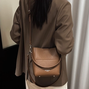 Detail einer dunkelbraunen Leder-Eimertasche mit Logo und Metallfüßen am Boden