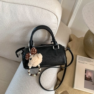 Detail of black Boston handbag with plush bear charm and silver hardware on a sofa