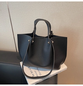 Close-up of black lychee-grain leather texture and golden metal rivet details on tote bag