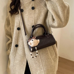 Close-up of a brown cylindrical Boston bag featuring a cute plush bear charm with beads