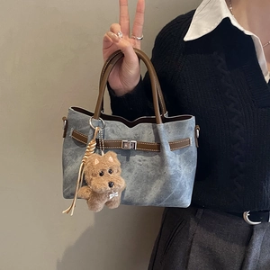 Detail of blue textured tote bag with brown leather handles and plush dog charm