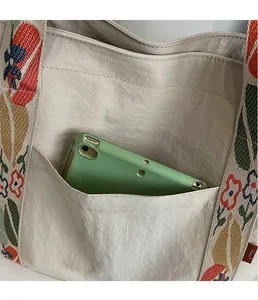 Close-up of off-white tote bag featuring a floral strap and a large functional front pocket