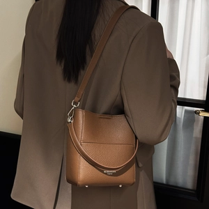 Detailansicht der braunen Beuteltasche aus Leder mit Narbung, Metallfüßen und Markenlogo