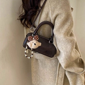 Detail of a dark brown leather Boston bag with a cute plush bear charm on a tweed coat