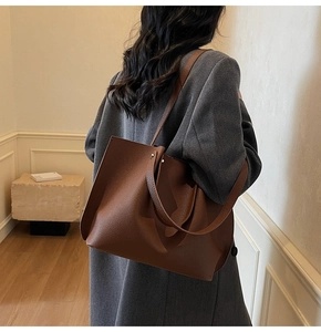 Close-up of a large brown textured leather tote bag worn over a dark grey wool coat