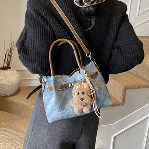 Detail of blue denim tote bag with brown leather straps and woven tassel charm