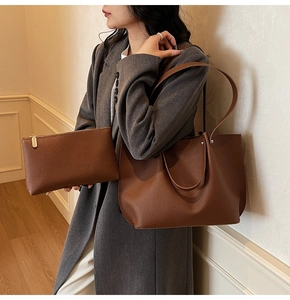Detail of deep brown pleated tote bag and pouch set styled on a gray blazer