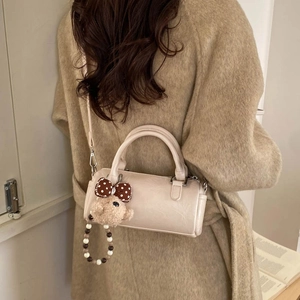 Detail of a beige cylinder bag with a cute bear pendant and a slim shoulder strap