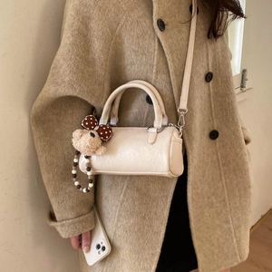 Close-up of cream cylinder handbag with leather texture and cute plush bear charm