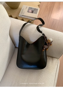 Close-up of black leather tote bag with a dachshund charm on a white sofa