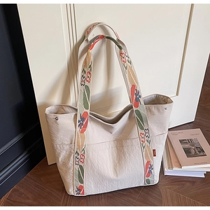 Detail of off-white tote bag with floral jacquard strap and side pocket by white door