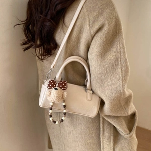 Detail of beige leather cylindrical handbag with cute plush bear charm on a beige coat