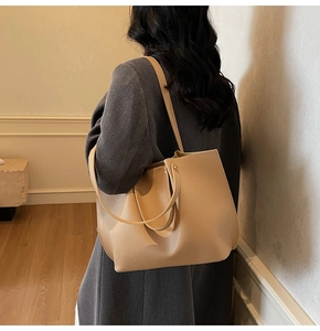 Detail view of large pleated tote bag in beige leather on a charcoal coat model