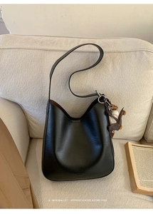 Detail of vintage black matte hobo bag with horse charm on a beige fabric sofa