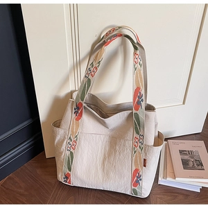 Close-up of beige canvas tote bag with floral embroidered handles and side pockets