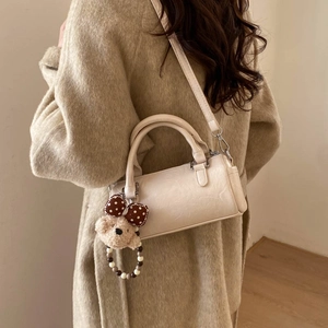 Detail of cream cylindrical crossbody bag with cute plush bear charm on soft leather