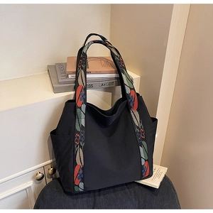 Detail of wide woven shoulder strap with retro floral embroidery on black tote bag