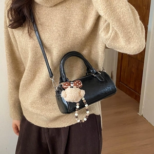 Close-up of black glossy cylindrical Boston bag with cute plush bear charm detail