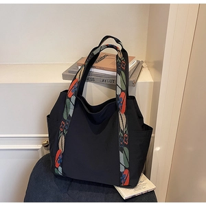 Detail of black tote bag featuring colorful floral jacquard strap and side pocket design