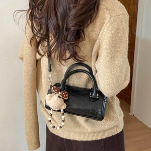 Detail of black pleated cylinder bag with shoulder strap and cute bear keychain charm