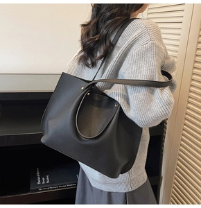 Detail of black pleated leather tote bag showing texture and long shoulder strap