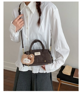 Detail of dark brown retro baguette bag with metal logo and plush doll pendant