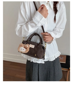 Detail of dark brown Boston handbag with round handles and plush animal charm