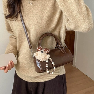 Detail of dark brown cylinder bag with plush bear charm and beaded strap accessory
