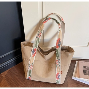 Detail of beige tote bag with vibrant floral embroidery on a wide shoulder strap