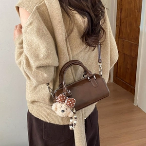 Brown glossy leather cylinder bag with cute plush bear charm shown on a model