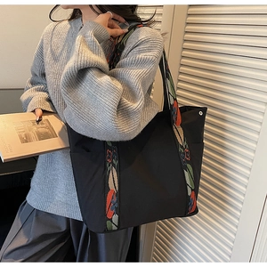 Detail of large black tote bag with colorful floral woven wide strap and silver side buttons